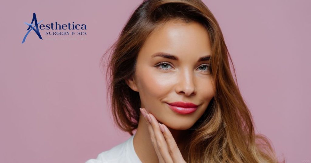 Young woman with long hair and pink lips gently touches her chin (model)