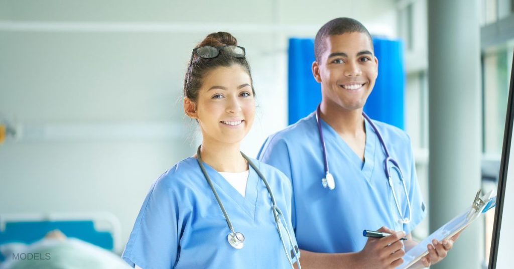 Two student doctors looking over and smiling. (MODELS)