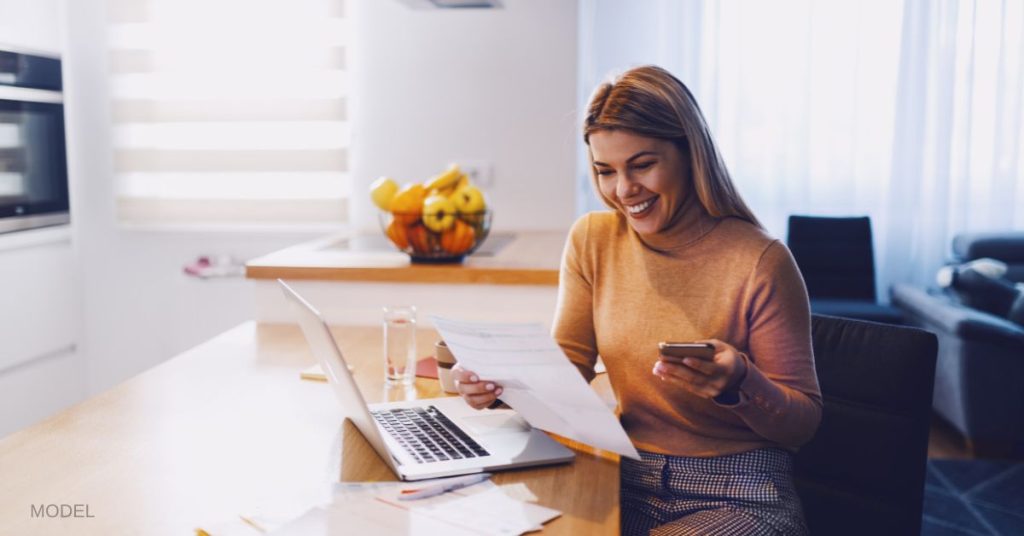 Woman sitting at the counter with laptop looking at papers. (MODEL)