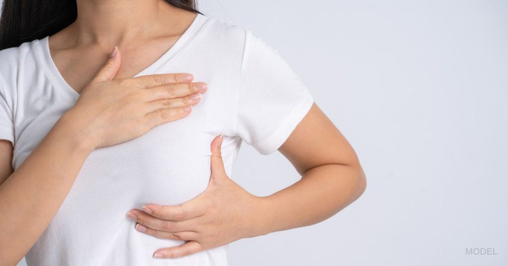 A woman in white shirt is giving herself a breast exam. (Model)