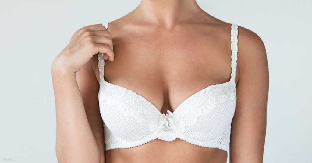 Woman wearing a white bra with one hand touching the strap on her shoulder (model)