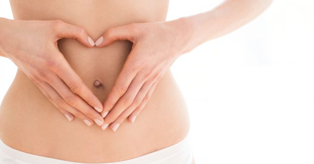 Woman holding her hands in the shape of a heart on her stomach (model)